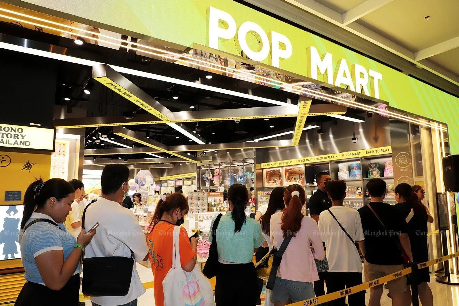 Фенове чакат на дълга опашка пред Pop Mart магазин с ярко осветена витрина и жълта декорация „Back to Play“.